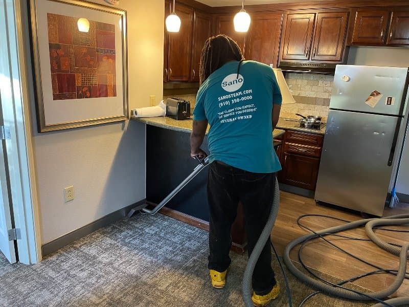Sano Steam technician in branded teal shirt steam cleaning carpet in a residential kitchen near Wilmington NC