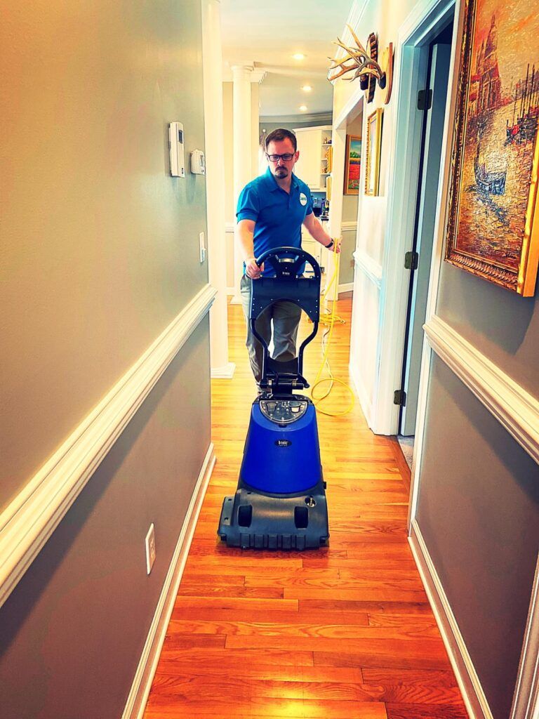 Sano Steam technician operating professional floor cleaning machine on hardwood floors in residential hallway