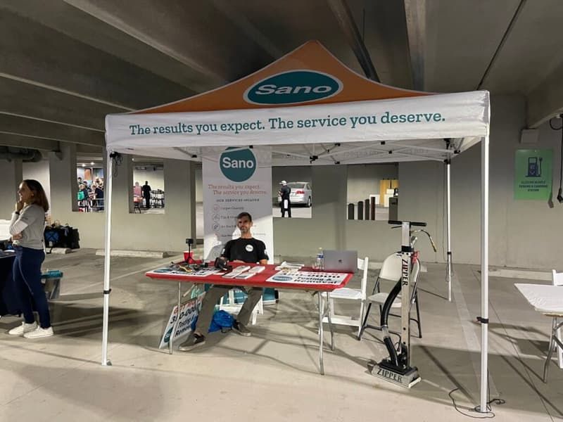 Sano Steam team member at a community event booth with branded tent, banner, and Zipper portable cleaning equipment in Wilmington NC