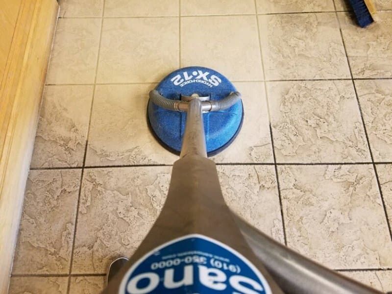 Sano Steam branded SX-12 tile spinner tool cleaning dirty grout lines on residential tile floor
