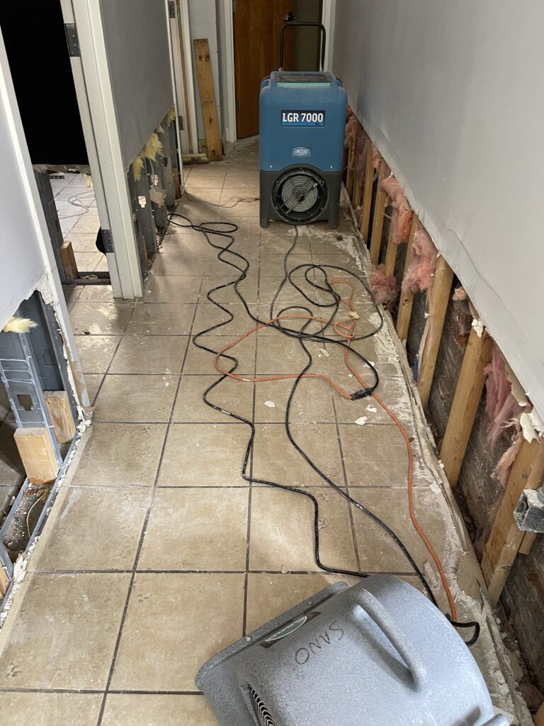 LGR 7000 commercial dehumidifier and Sano Steam air mover drying water-damaged hallway with exposed wall framing